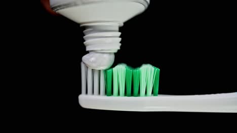 A-toothbrush-being-loaded-with-some-toothpaste,-dark-background