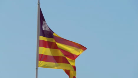 Real-fabric-flag-of-Balearic-Islands-an-autonomous-community-in-Spain,-waving-in-the-wind-against-a-blue-sky