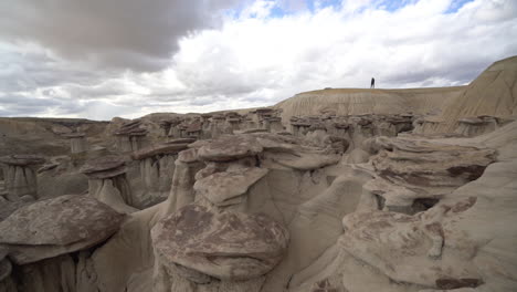 Lonely-Human-Figure-Walking-on-Top-of-the-Cliff-Above-Mushroom-Sandstone-Formations-in-Bisti-De-Na-Zin-Wilderness,-New-Mexico-USA