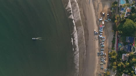 Descending-top-down-aerial-as-lone-fishing-boat-leaves-beach-in-morning,-4K