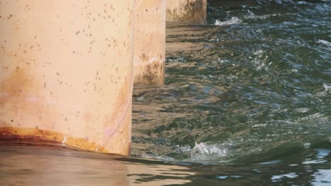 Orange-concrete-bridge-pilings-with-river-water-current-rushing-past