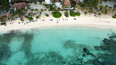 Aerial-bird's-eye-drone-view-of-a-beautiful-tropical-vacation-beach-with-crystal-clear-blue-water,-white-sand,-palm-trees,-lounge-chairs-at-a-resort-in-Riviera-Maya,-Mexico-near-Cancun