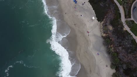 Top-down-shot-of-the-wave-on-Laguna-Beach-tilting-up-towards-a-hotel-beach-resort