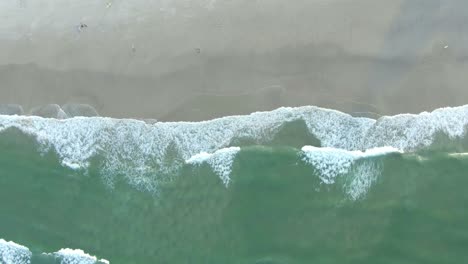 Aerial-spinning-drone-view-of-sea-waves-breaking-on-sandy-coastline