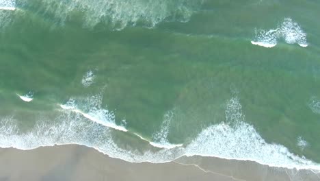 Aerial-top-down-view-of-sea-waves-breaking-on-sandy-coastline