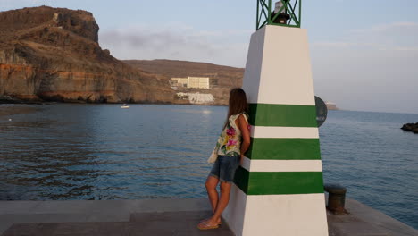 Junge-Frau-Ruht-Auf-Einer-Seelampe-Und-Beobachtet-Die-Bucht-Und-Die-Küstenklippe-Auf-Den-Kanarischen-Inseln