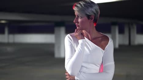 Beautiful-white-caucasian-short-haired-blonde-women-acting-nervous-scared-in-underground-car-parking-lot-in-white-dress-with-red-light-behind-her