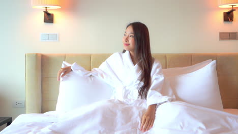 Happy-woman-lying-on-the-bed-in-white-bathrobe-dreaming-looking-at-the-window-daytime