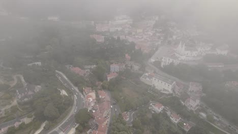 Dramatic-aerial-descending,-breaking-through-the-fog-reveals-town-palace-and-townscape-of-Sintra
