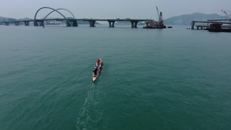 Dragon-Boat-team-rowing-to-the-pace-of-an-onboard-Drummer,-Aerial-view