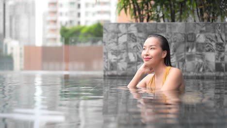 A-young-attractive-Asian-woman-relaxing-inside-an-outdoor-rooftop-swimming-pool-at-Spa-resort,-thinking-face-close-up-slow-motion-side-view