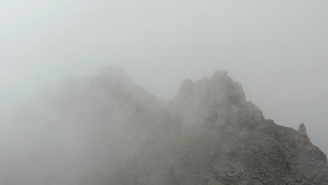 Volando-Sobre-La-Cumbre-De-La-Montaña-Rocosa-Cubierta-De-Niebla-Espesa