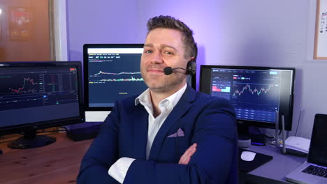 Portrait-of-a-happy-successful-forex-cryptocurrency-trader-analyst-broker-smiling-in-his-office-with-stock-market-graphs-on-screens-behind-him