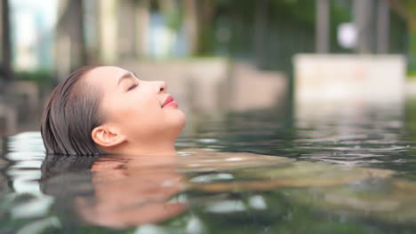 Close-up-of-young-Asian-woman-floating-on-back-and-relaxing-in-warm-pool-of-luxury-resort-or-spa