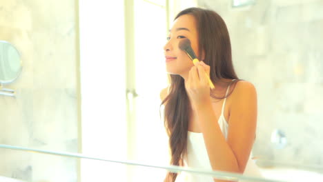 Asiatische-Frau-Trägt-Hautpuder-Mit-Einem-Pinsel-In-Ihrem-Badezimmer-Auf-Das-Gesicht-Auf,-Reflexion-Im-Spiegel