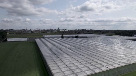 Ascending-aerial-movement-showing-greenhouse-with-countenance-cityscape-of-Zutphen-in-the-background-with-and-cumulus-clouds-against-a-blue-sky-above