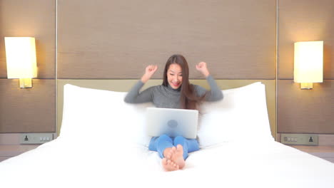 Woman-sitting-barefoot-in-bed-using-laptop-cheers-when-she-wins-a-game