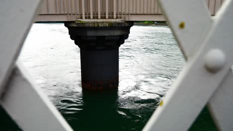Sea-water-splashing-beneath-submerged-concrete-bridge-foundation-view-through-railings-dolly-left