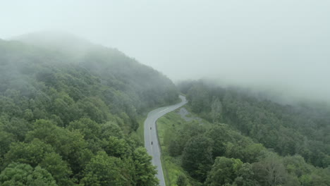 Aerial-following-motorcycles-moving-fast-down-windy-foggy-mountain-road,-4K