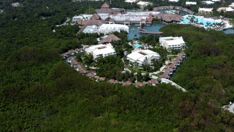 Beautiful-spinning-aerial-drone-shot-of-a-group-of-bungalows-and-larger-buildings-surrounded-by-a-mangrove-forest-in-a-tropical-vacation-resort-in-Riviera-Maya,-Mexico-near-Mexico