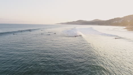 Aerial-as-surfers-paddle-out-during-beautiful-sunrise-tropical-coast,-4K