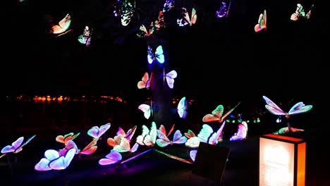 Colorful-animatronic-butterflies-sit-are-scattered-on-the-ground-and-in-a-tree-while-opening-and-closing-their-wings