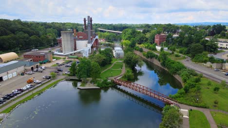 Aerial-drone-footage-of-the-river-walk-park,-the-chadakoin-river,-and-an-industrial-area-of-downtown-Jamestown,-New-York,-during-summer-with-a-pedestrian-bridge