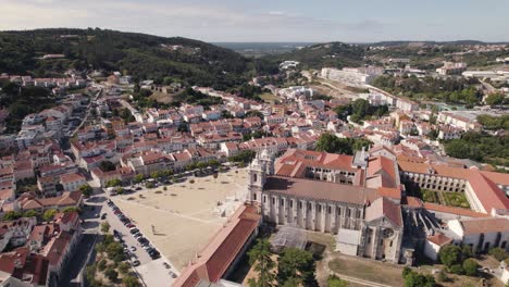 Orbiting-shot-of-Mosteiro-de-Alcobaça-against-cityscape-and-forest,-Portugal