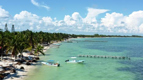 Aerial-drone-dolly-in-flying-shot-of-a-small-fishing-town-in-the-nature-reserve-of-Sian-Ka'an-near-Tulum,-Mexico-with-small-fishing-boats,-piers,-palm-trees,-and-white-sand-on-a-summer-day