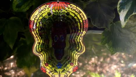 Hypnotic-metal-sugar-skull-ornate-colourful-spinning-garden-ornament-hanging-from-tree