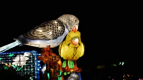 Two-light-animatronic-parrots-move-their-winds-and-beaks-against-a-dark-night-sky