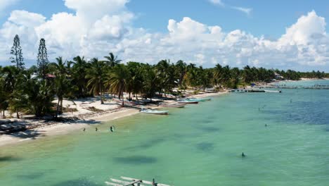 Aerial-drone-trucking-right-shot-of-the-coast-of-a-small-fishing-town-in-the-nature-reserve-of-Sian-Ka'an-near-Tulum,-Mexico-with-small-fishing-boats,-piers,-palm-trees,-and-white-sand-on-a-summer-day