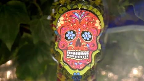 Hypnotic-metal-sugar-skull-decorative-colourful-spinning-garden-ornament-hanging-from-tree-closeup-shot