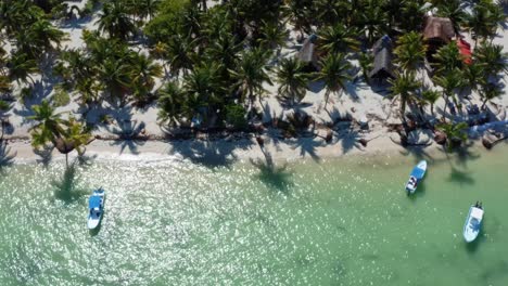 Aerial-drone-bird's-eye-top-view-of-the-coast-of-a-small-fishing-town-in-the-nature-reserve-of-Sian-Ka'an-near-Tulum,-Mexico-with-small-fishing-boats,-piers,-palm-trees,-and-white-sand-on-a-summer-day