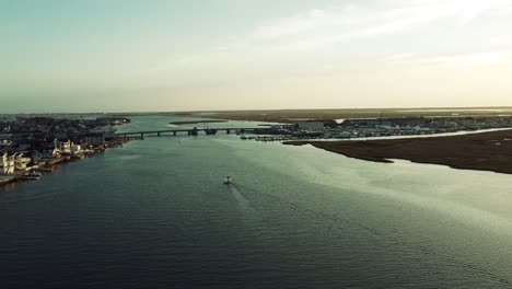 Ariel-over-the-Harbor-headed-towards-the-bridge-in-Stoneharbor,-New-Jersey-with-a-small-boat-in-the-center-during-golden-hour