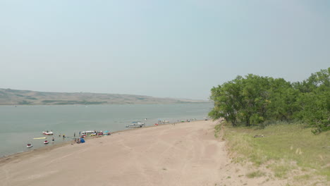 Wide-aerial-pan-of-people-and-boats-on-beach-at-Saskatchewan-Landing,-Canada