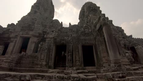 Historical-building-facade-of-Bayon-Temple-within-Angkor-complex,-Cambodia,-tilting-upward-shot