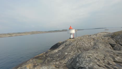 Dangerous-low-altitude-flying-over-rocky-island-toward-small-lighthouse,-FPV-drone