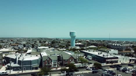 Aerial-flyover-the-beach-houses-of-Stone-Harbor,-New-Jersey-with-the-water-tower-in-the-Atlantic-ocean-on-the-horizon