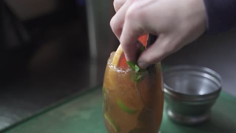 Close-up-of-Bartender-adding-mint-leaf-on-top-of-alcoholic-Cynar-Drink-in-glass-at-party,slow-motion