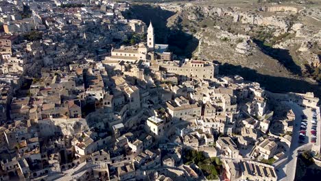 Drone-zooming-out-from-hills-of-ancient-city-Matera-in-Italy,-church-in-the-middle-of-the-shot