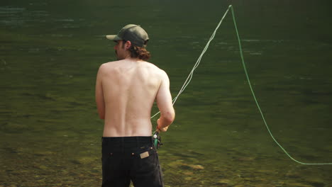 Caucasian-guy-fly-fishing-at-a-flowing-river-in-McDonald-Creek,-medium-shot