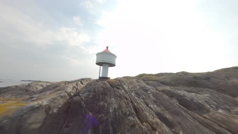 Majestic-tiny-lighthouse-with-red-rooftop-on-rocky-island,-closeup-FPV-drone-flyby-and-orbit