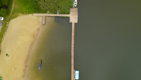 Ascend-top-down-of-sandy-beach-and-wooden-jetty-during-sunny-day-at-Hartowiec-Lake-in-Poland