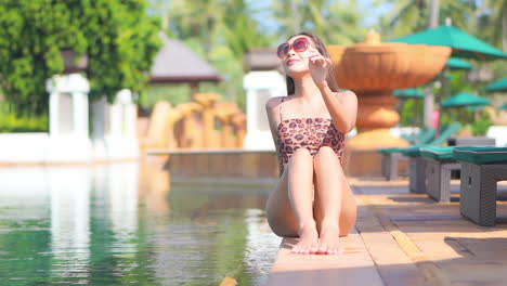 Amerikanische-Frau-Im-Fleckigen-Badeanzug,-Die-Am-Rand-Des-Schwimmbades-In-Einem-Exotischen-Tropischen-Hotel-In-Hawaii-Sitzt