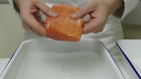 Male-chef-washing-and-cleaning-fresh-salmon-fillet-in-restaurant-kitchen,close-up