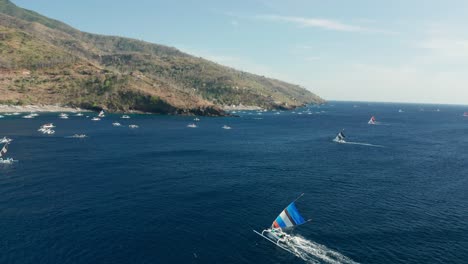 Colorful-sail-boat-traveling-towards-shore-of-Bali,-blue-ocean