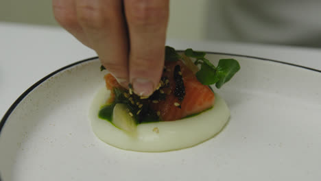 Close-up-shot-of-starred-chef-adding-sesame-and-seaweed-on-salmon-meal