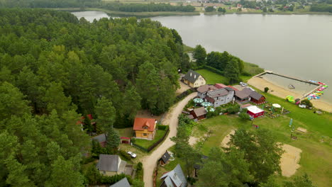 Aerial-View-Of-Green-Forest,-Cabin,-Beach,-And-Lake-In-Hartowiec,-Poland
