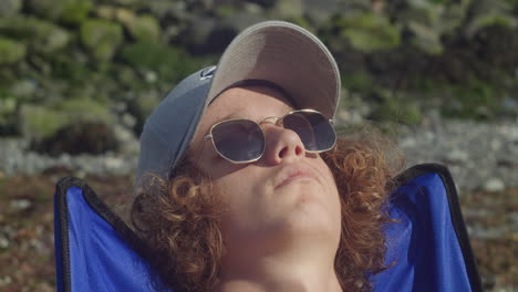 Close-Up-Of-Male-Tourist-In-Cap-And-Sunglasses-Relaxing-Under-The-Sunlight-At-The-Beach